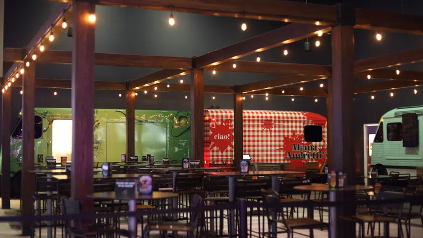 Outdoor dining area with string lights and colorful food trucks in the background at night.