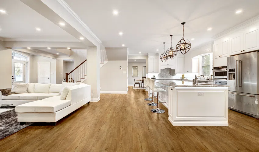 Modern open concept living room and kitchen with white cabinets, wooden floors, and stylish pendant lighting.