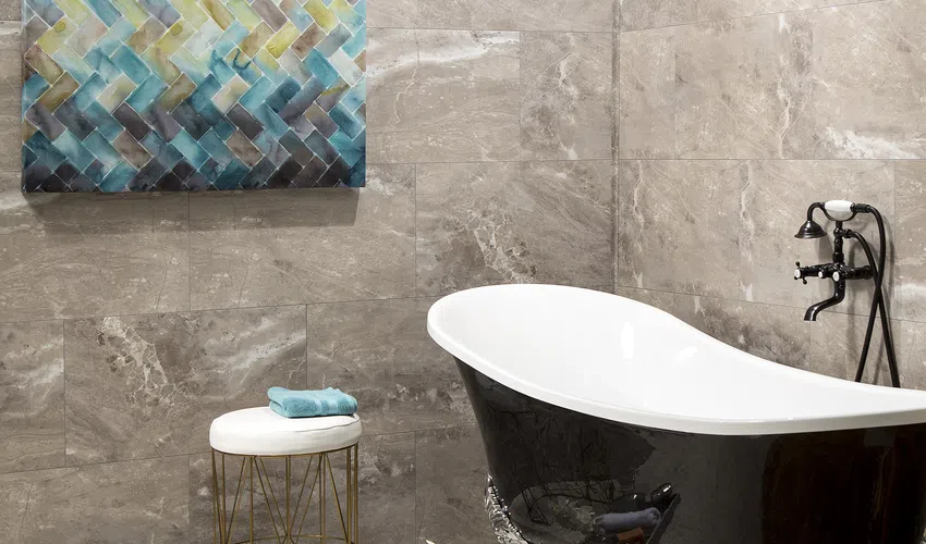 Elegant bathroom with a black clawfoot tub, beige marble tiles, abstract wall art, and a stool with towels.