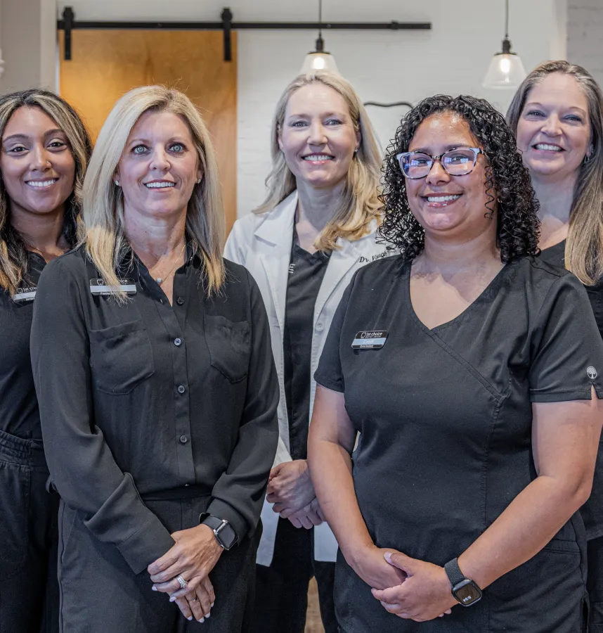 A group of five healthcare professionals in black attire smiling in a modern clinic setting.
