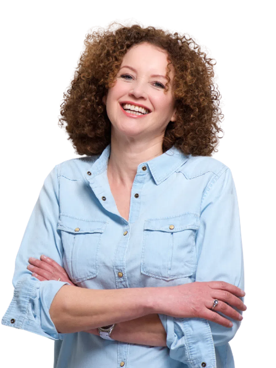 Smiling woman with curly hair wearing a light blue denim shirt, arms crossed confidently.
