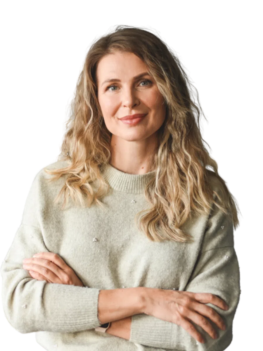 Smiling blonde woman with wavy hair wearing a light gray sweater with arms crossed confidently