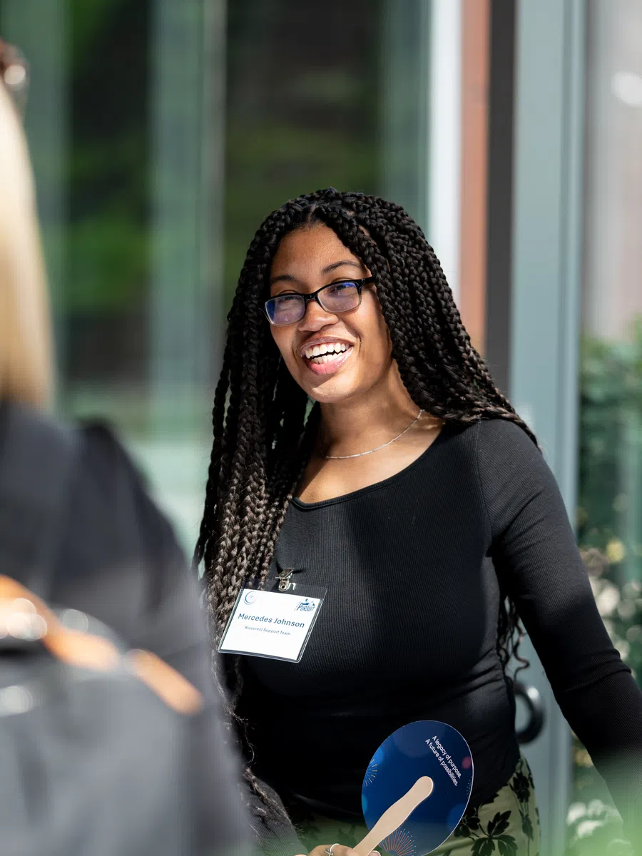 Smiling woman with braided hair and glasses engaging in conversation outdoors during daytime event