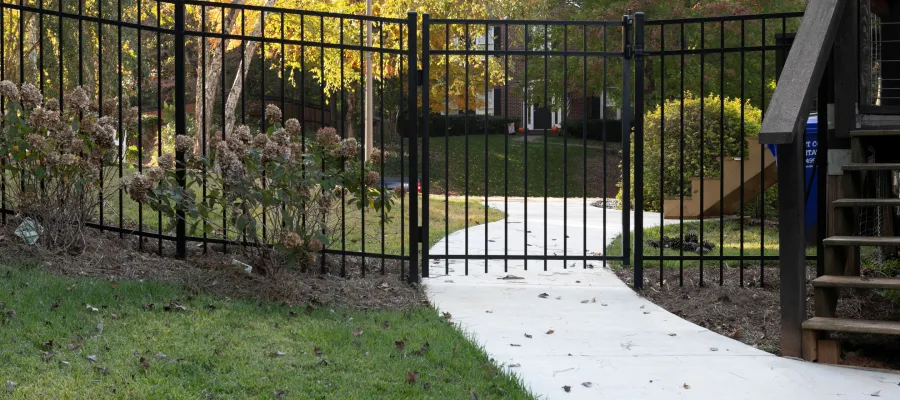A black metal gate leads to a serene pathway in a lush, green landscaped area.