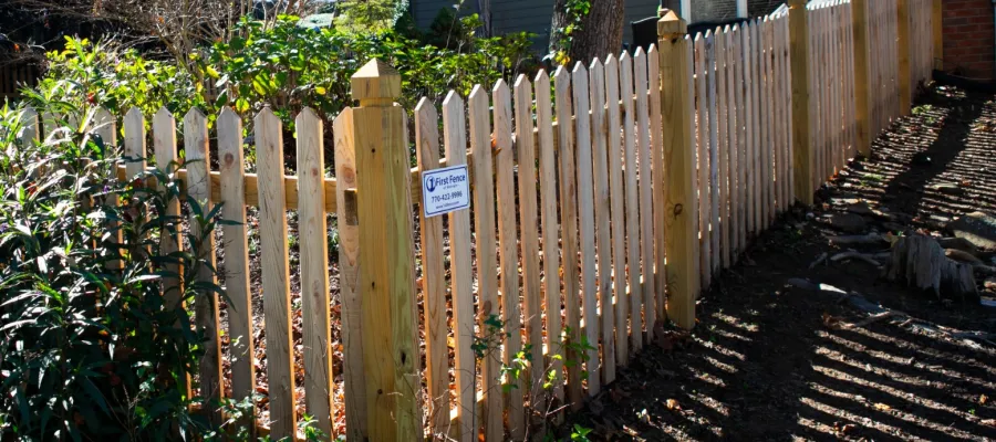 A well-maintained wooden fence surrounding a garden, with greenery and shadows cast by sunlight.