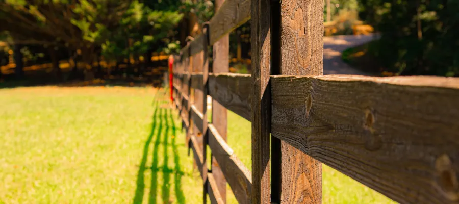 Close-up of a rustic wooden fence casting long shadows on vibrant green grass under sunlight.