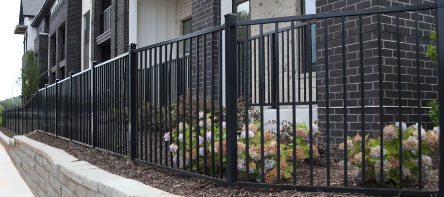 Black metal fence along a landscaped raised garden bed in front of modern brick townhouses