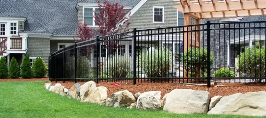 Black metal fence with landscaping, rocks, and a modern home in the background, showcasing a well-maintained yard.