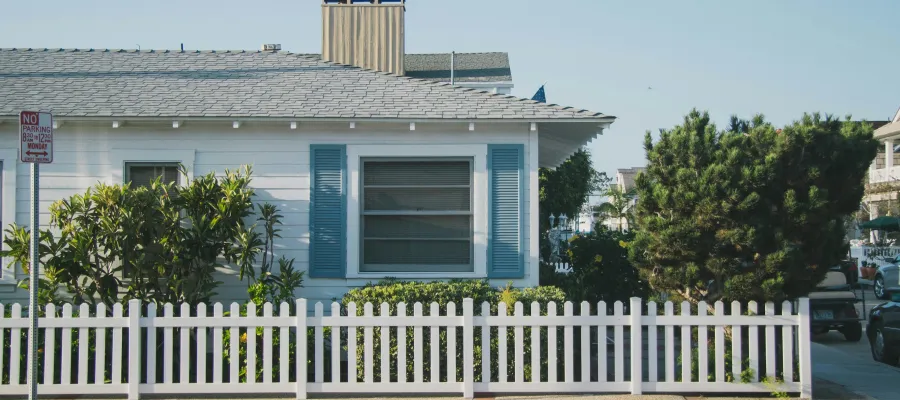 Charming house with blue shutters, white picket fence, and lush landscaping on a sunny day.