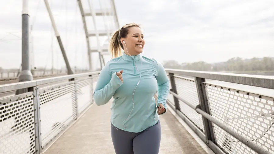 Woman in athletic wear jogging on a bridge outdoors in cloudy weather with earphones in ears