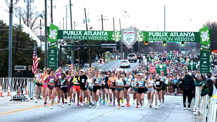 Runners starting the Publix Atlanta Marathon weekend race under green start banner on city road.