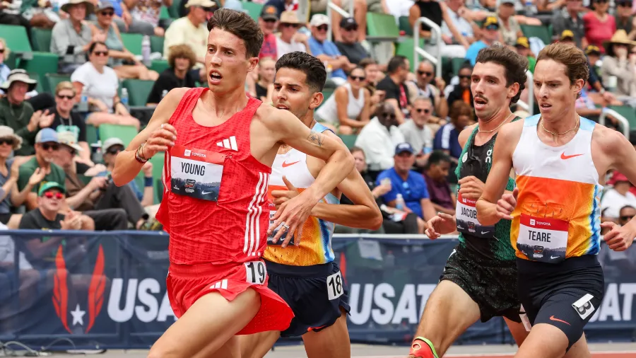 Four male athletes sprinting intensely on a track during a competitive race with a crowded audience in the background