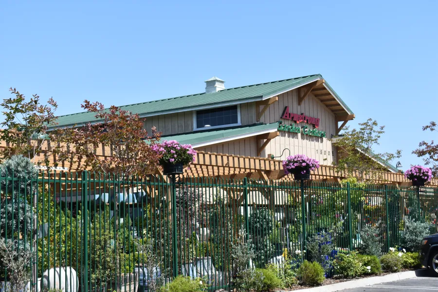 Exterior view of a garden center with green fencing, blooming flowers, and plants under a clear blue sky.