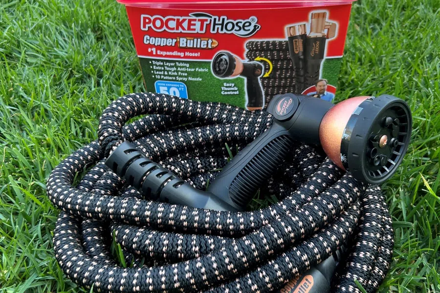 Coiled black and copper Pocket Hose with spray nozzle on green grass next to red storage container