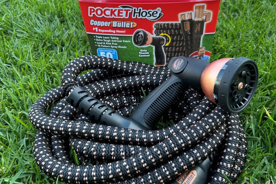 Coiled black and copper Pocket Hose Copper Bullet expandable garden hose with spray nozzle on green grass.