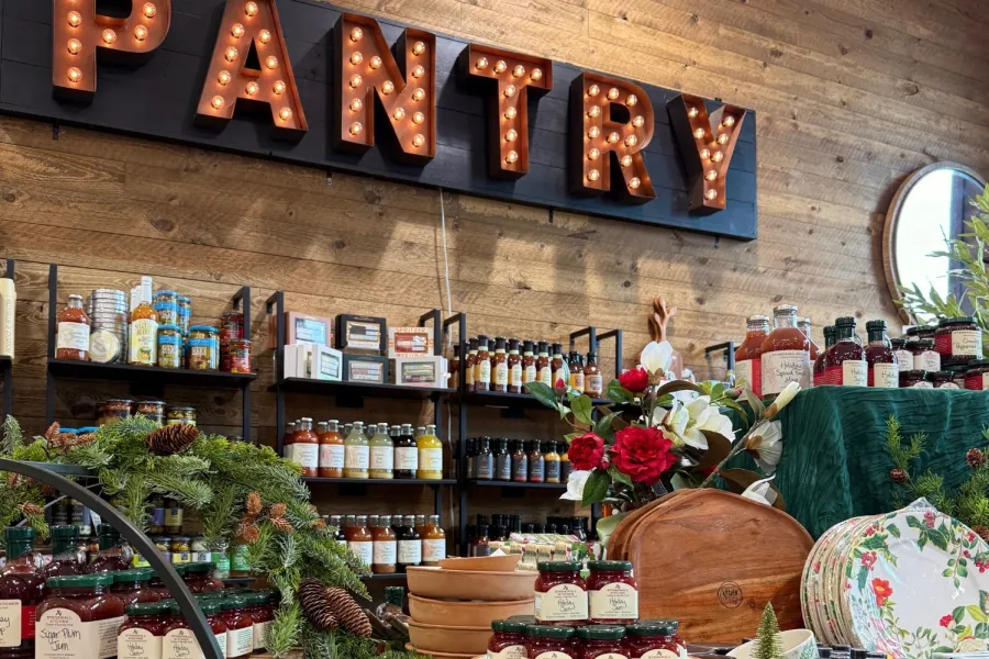 Festive pantry display with jams, cookie cutters, floral decor, and holiday-themed kitchenware on green tablecloth.