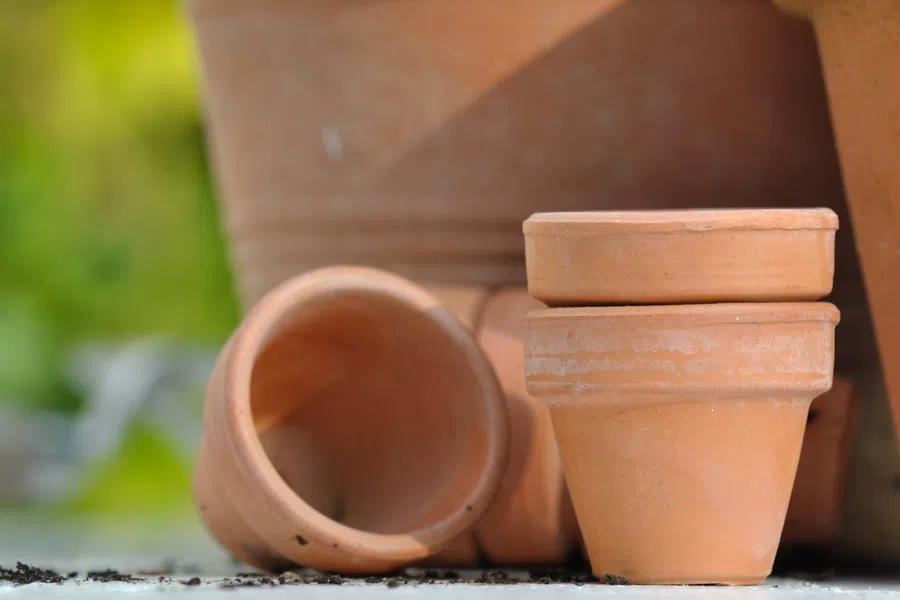Stacked and scattered empty terracotta plant pots on a surface with blurred green background.