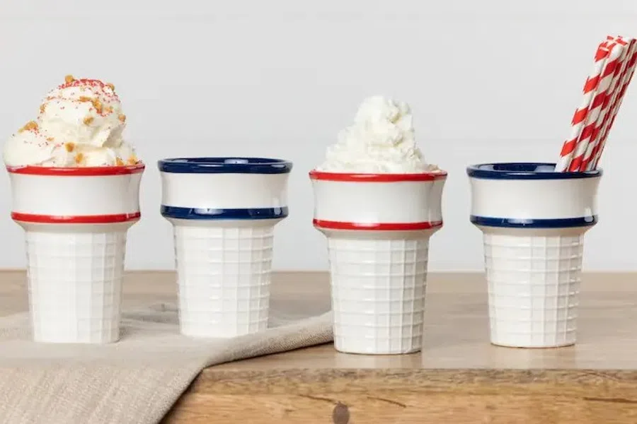 Four ceramic cups with waffle cone texture, two topped with whipped cream and two plain, on wooden surface.