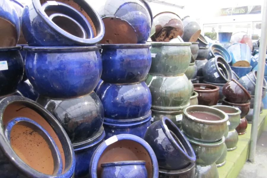 Stacks of blue and green glazed ceramic pots displayed in a garden center or nursery.