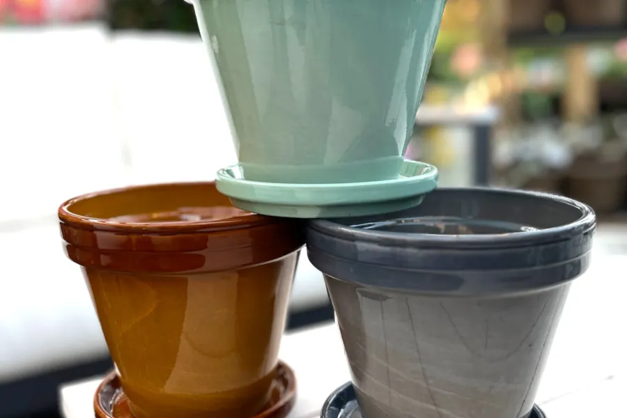 Three glazed ceramic plant pots in brown, gray, and light blue stacked on a wooden table outdoors.