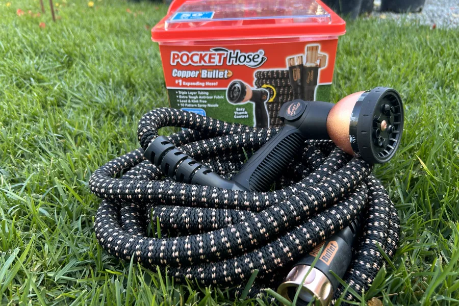 Pocket Hose Copper Bullet expanding garden hose coiled on grass with red storage container and spray nozzle