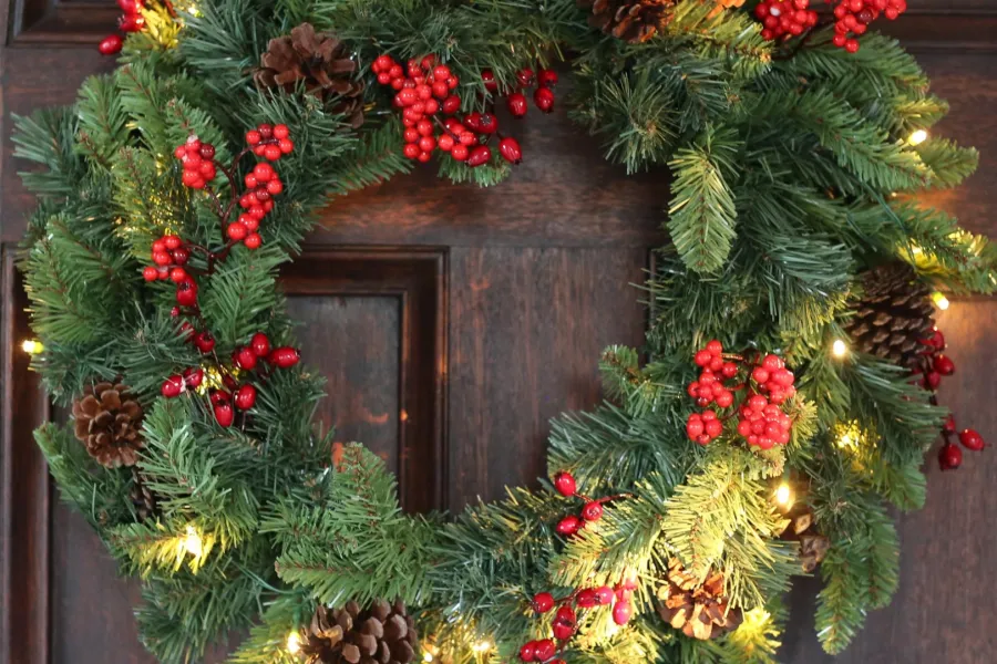 Festive Christmas wreath with pinecones, red berries, and warm string lights on a wooden door.