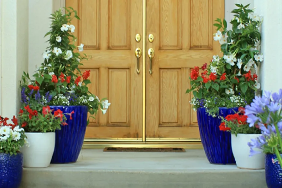 red, white a blue flowers in pots by a front door