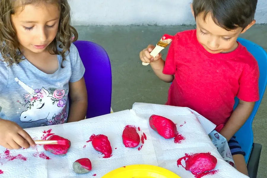 girl and boy painting rocks red