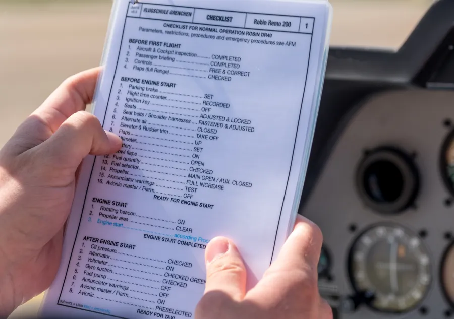 A pilot in the cockpit holding a laminated preflight checklist