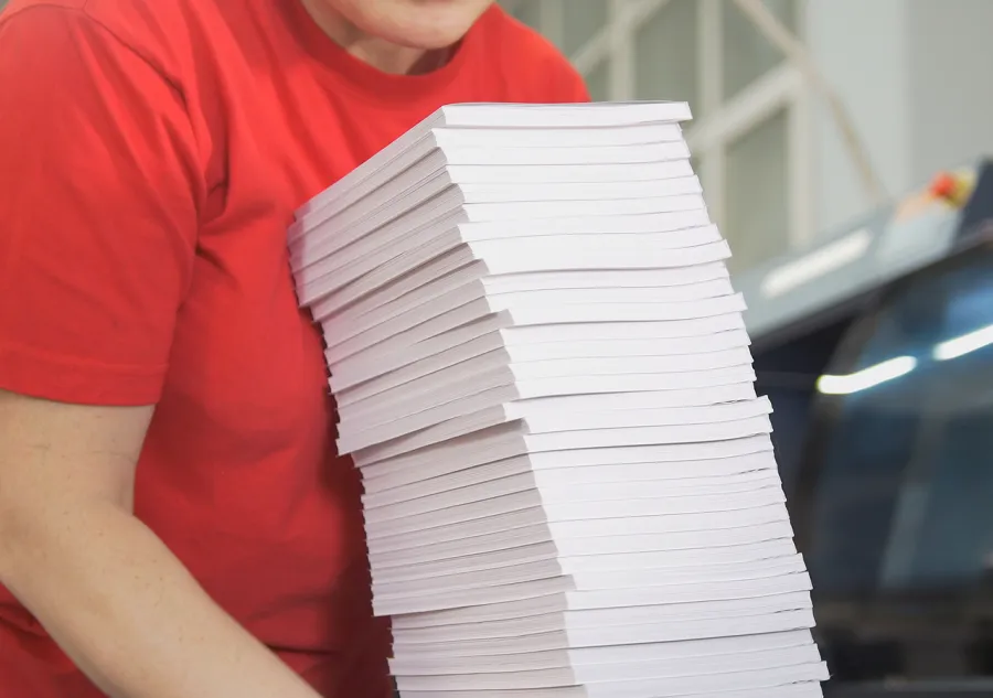 A printing plant worker holding a large stack of Perfect Bound books