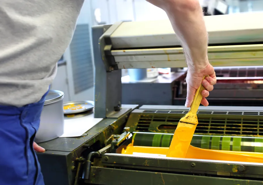 Man adding yellow ink to an offset printing press