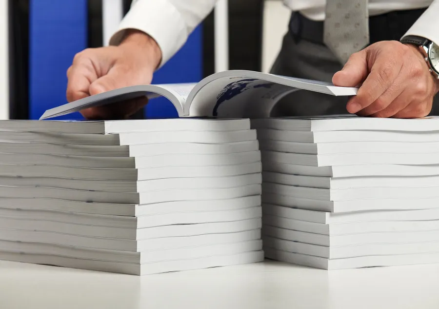 A man holding an open book over two stacks of books