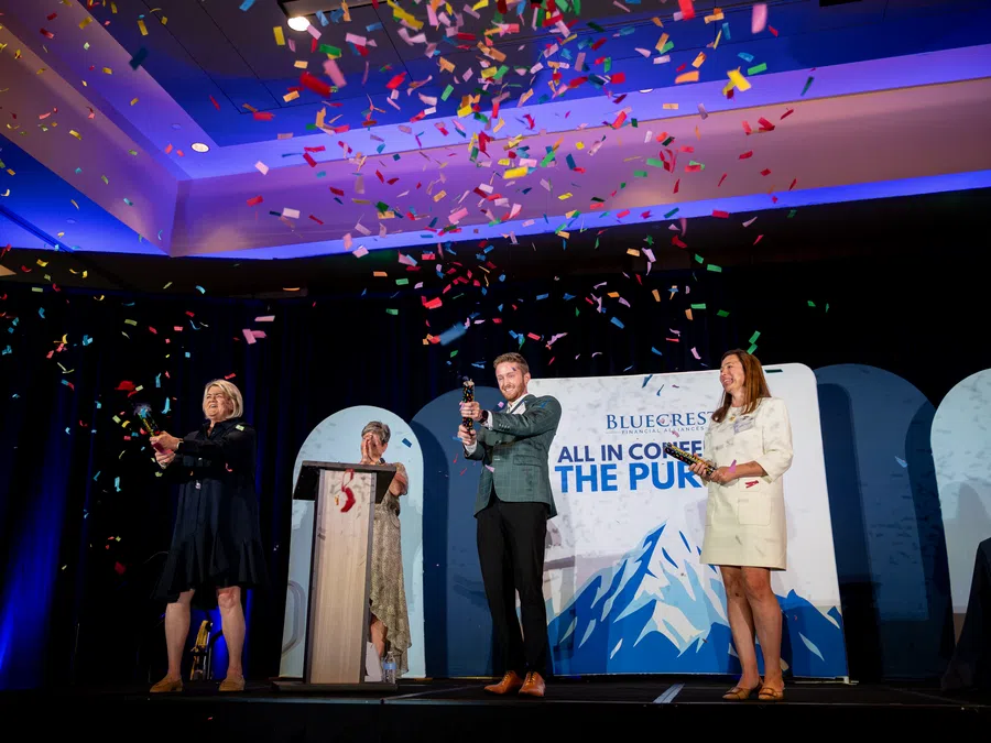 People celebrate on stage with confetti at a Blue Cross Blue Shield event under blue and purple lighting.