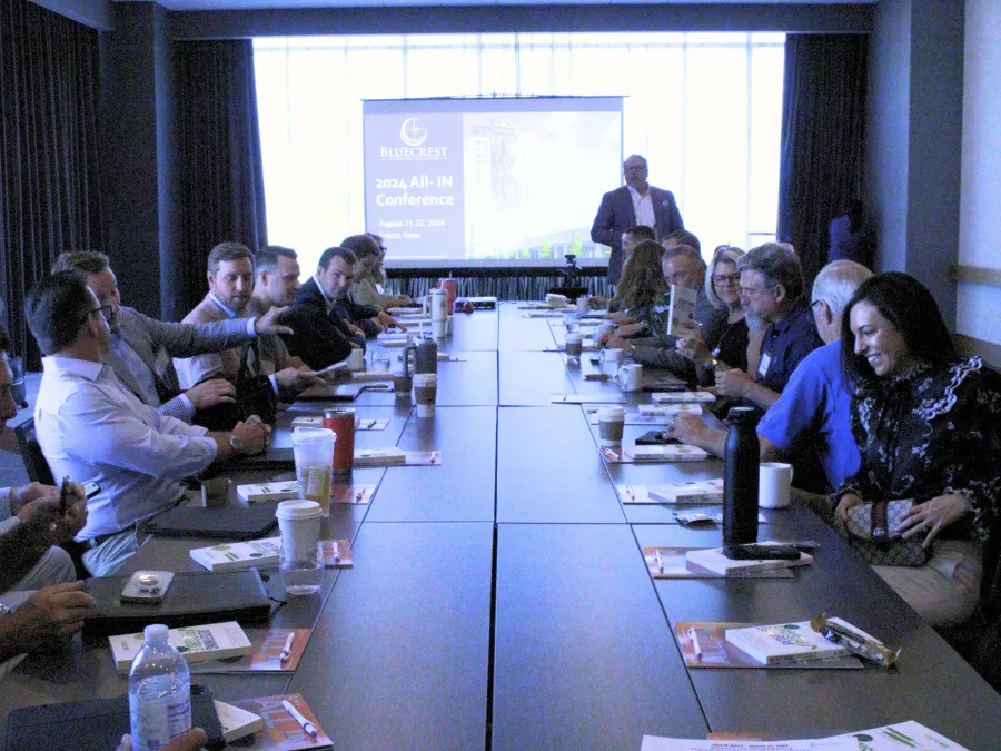 a group of people sitting at long tables in front of a screen