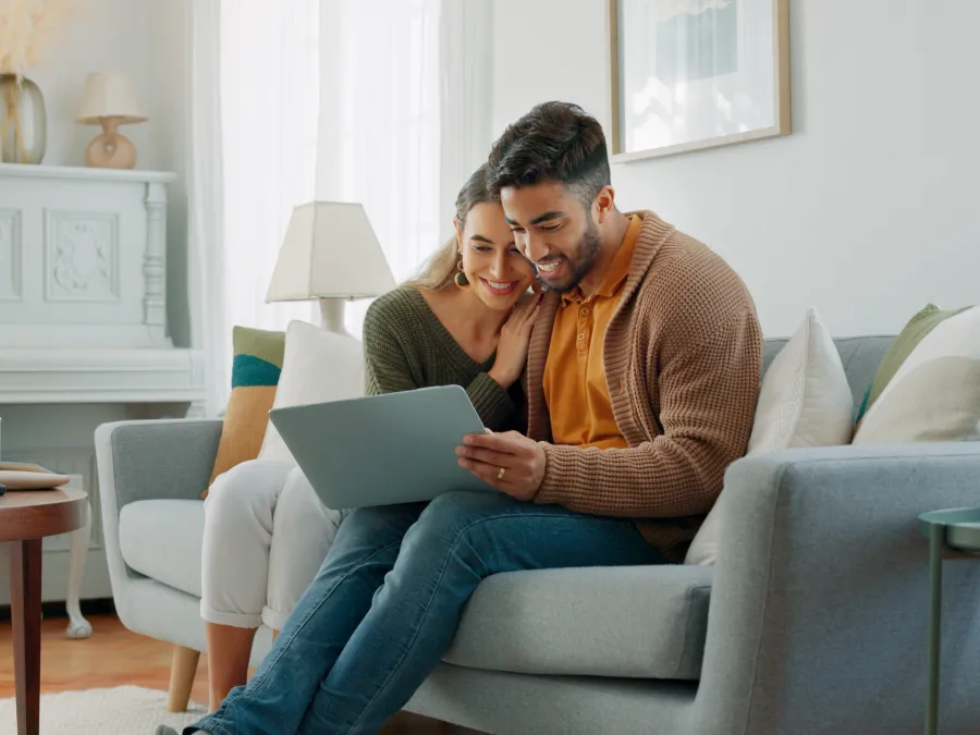 a man and woman sitting on a couch looking at a laptop