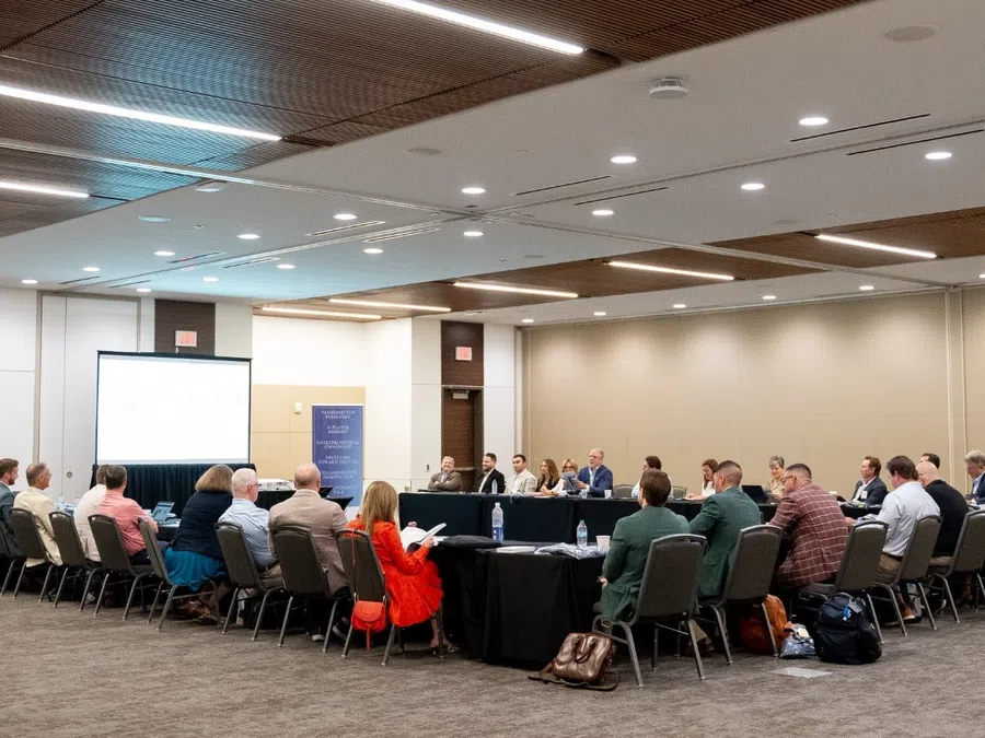 Business meeting with people seated around a large U-shaped table in a spacious conference room.