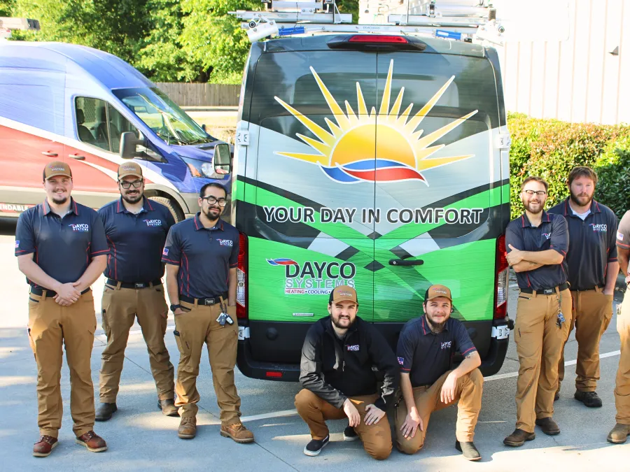 Team of nine technicians posing in front of a Dayco Systems service van with a sun logo and slogan your day in comfort