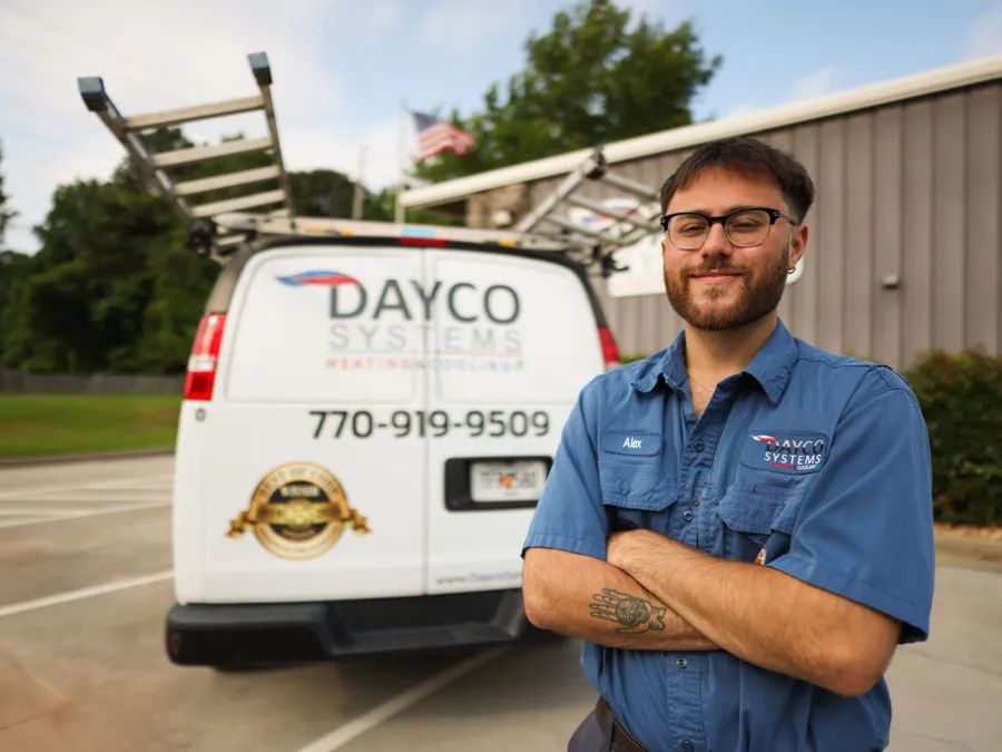 Dayco Systems technician with folded arms stands in front of a branded service van with ladders and phone number.