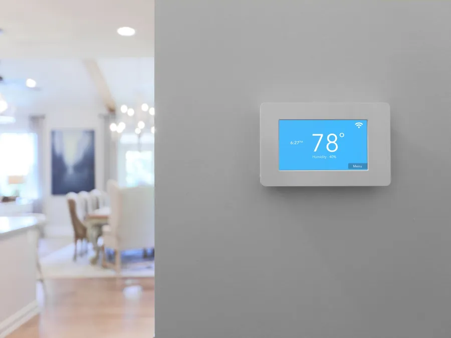 Smart thermostat on a gray wall displaying 78 degrees in a modern bright home interior.