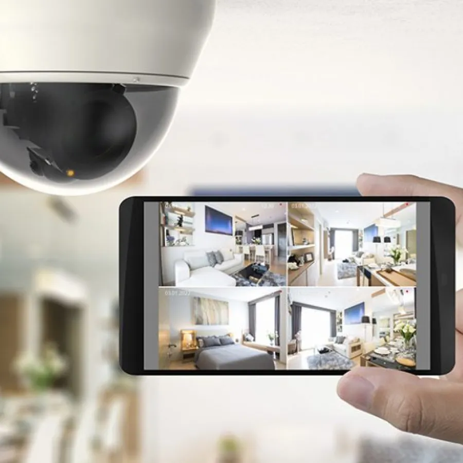 Smartphone displaying home security camera footage indoors under a dome camera capturing multiple room views