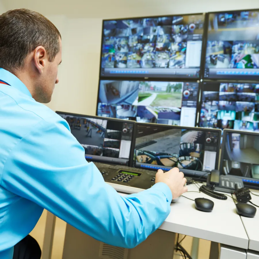 Security guard monitoring multiple surveillance camera feeds on several screens in control room