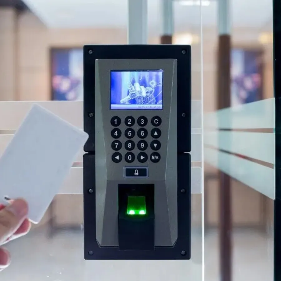 Hand holding an access card near electronic keypad and fingerprint scanner on glass door