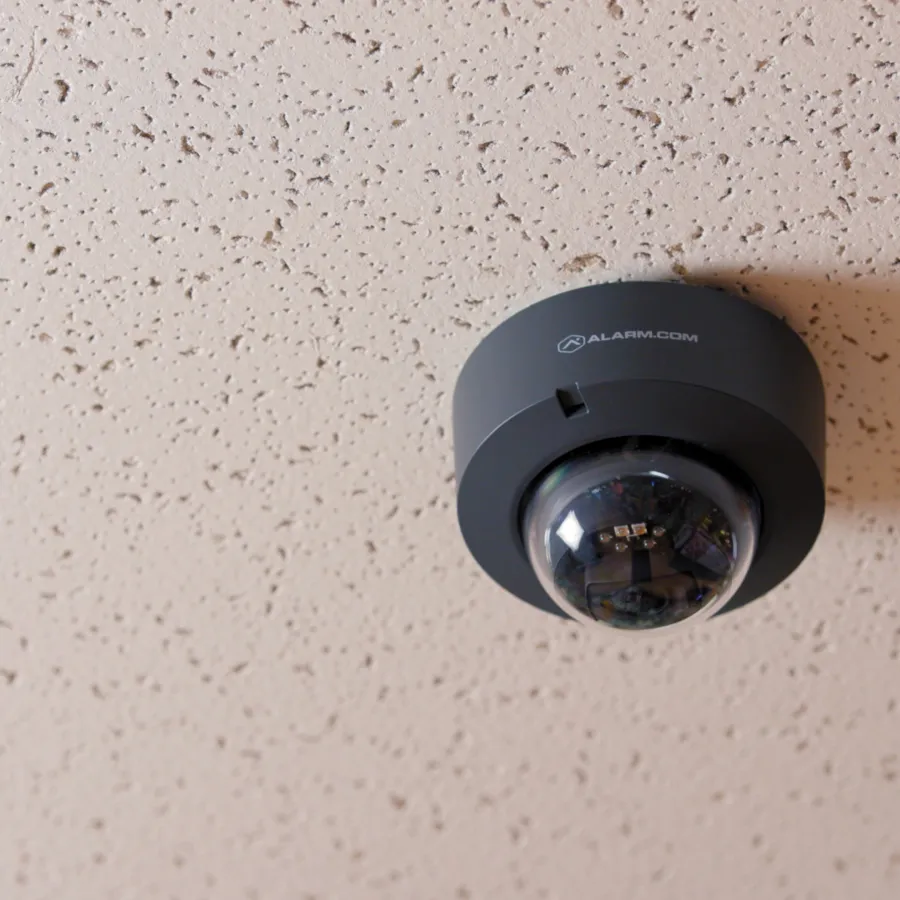 Black dome security camera mounted on textured white ceiling for indoor surveillance.