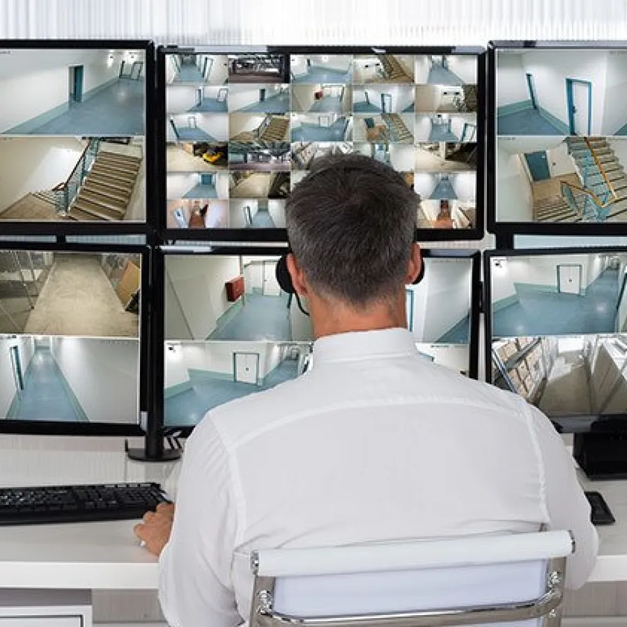 Security guard monitoring multiple surveillance camera feeds on six screens
