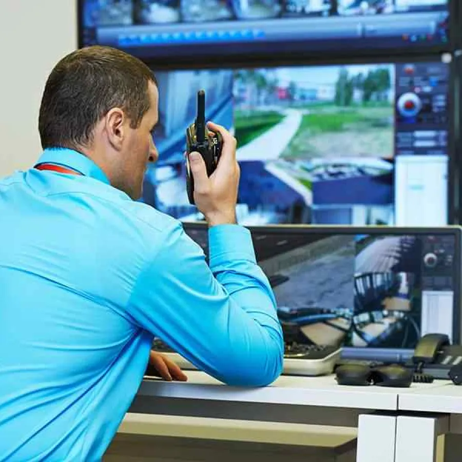 Security guard monitors multiple surveillance screens while communicating through a walkie-talkie in control room