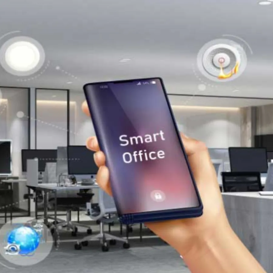 Hand holding smartphone displaying Smart Office app controlling devices in a modern office workspace environment.