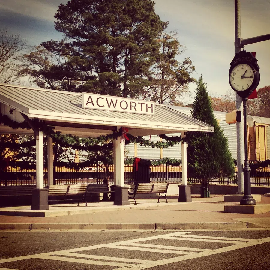 Acworth train station shelter decorated with garlands and clock on sunny day with trees in background