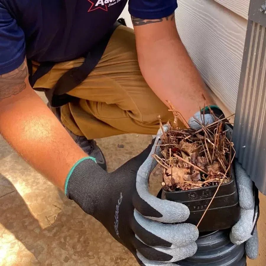 A person wearing gloves cleans debris from a home’s gutter system, ensuring proper water flow.