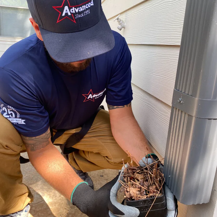 A technician removing debris from a downspout for proper drainage maintenance.