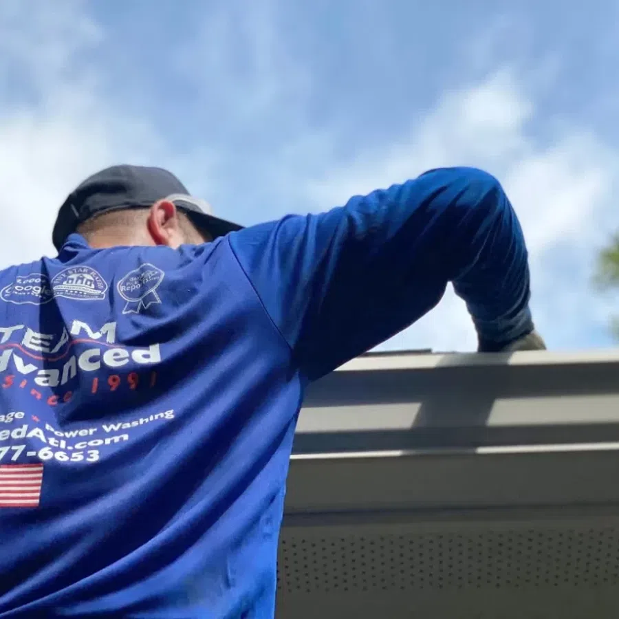 A worker in a blue shirt cleaning a roof gutter under a bright sky, representing professional maintenance services.